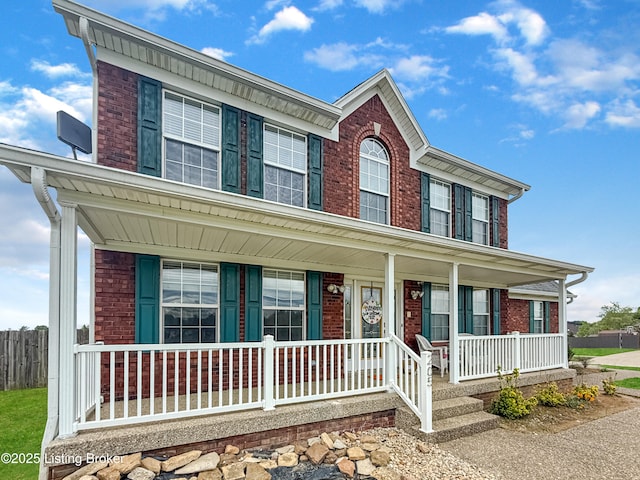 view of front of property with a porch, brick siding, and fence