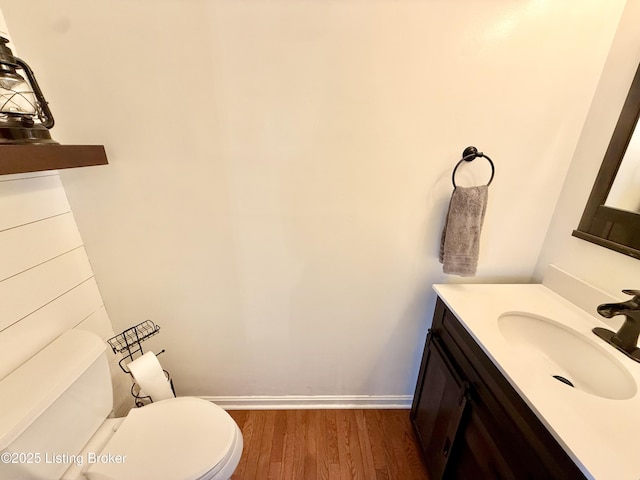 half bath with wood finished floors, vanity, toilet, and baseboards