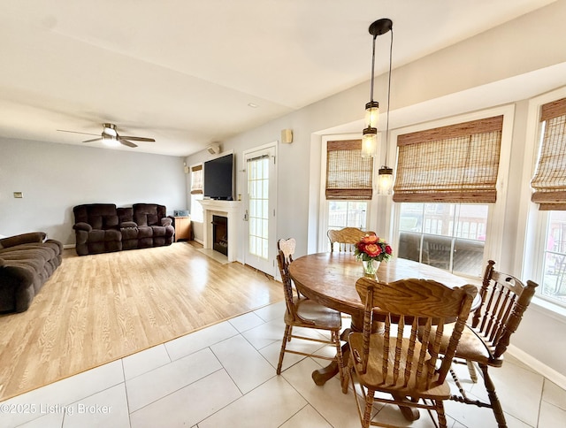 dining room featuring light tile patterned floors, a ceiling fan, a fireplace, and baseboards