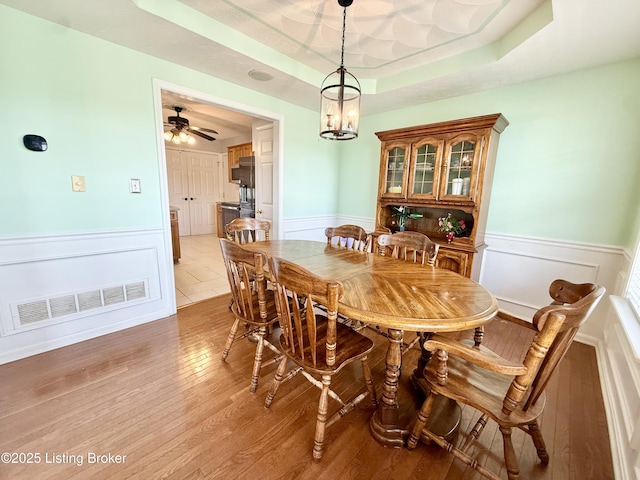 dining space with a wainscoted wall, light wood-type flooring, a tray ceiling, and a decorative wall