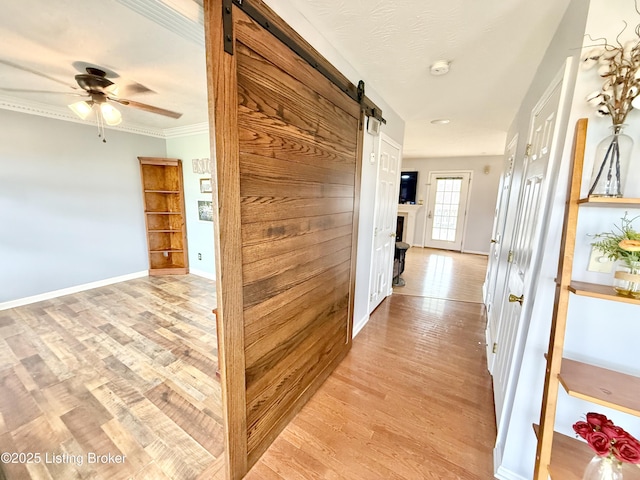 corridor featuring a barn door, light wood-style floors, baseboards, and ornamental molding