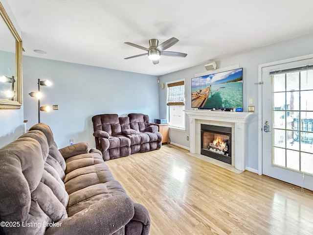 living area featuring a fireplace with flush hearth, a ceiling fan, wood finished floors, and baseboards