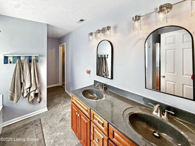 full bathroom with baseboards, double vanity, marble finish flooring, and a textured ceiling