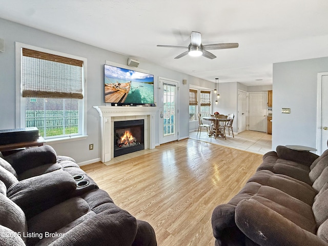 living area with ceiling fan, a fireplace, light wood-style flooring, and baseboards