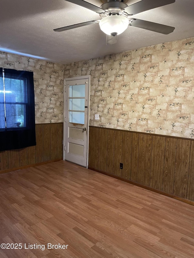 1310 Lacona Ln, Louisville, KY 40213 - unfurnished room featuring wainscoting, light wood-style floors, wooden walls, a ceiling fan, and a textured ceiling