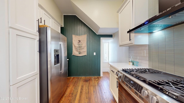 1228 S Floyd St, Louisville, KY 40203 - kitchen featuring stainless steel appliances, wall chimney exhaust hood, light wood finished floors, white cabinets, and tasteful backsplash