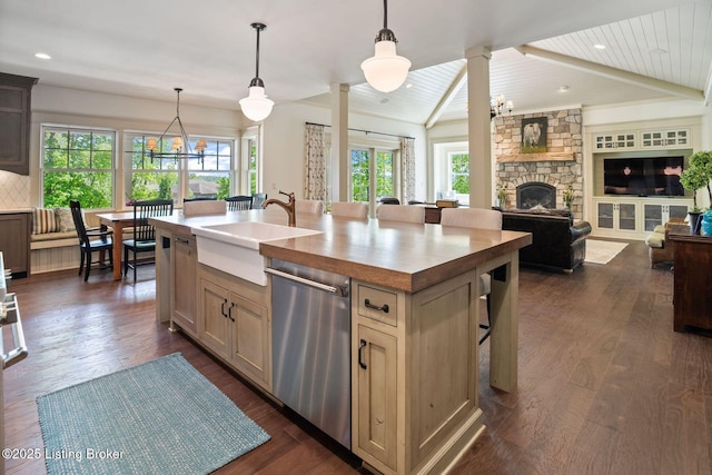 kitchen featuring stainless steel dishwasher, a chandelier, a sink, a stone fireplace, and an island with sink