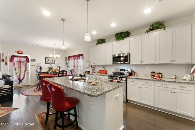 kitchen featuring appliances with stainless steel finishes, backsplash, white cabinets, a center island with sink, and recessed lighting