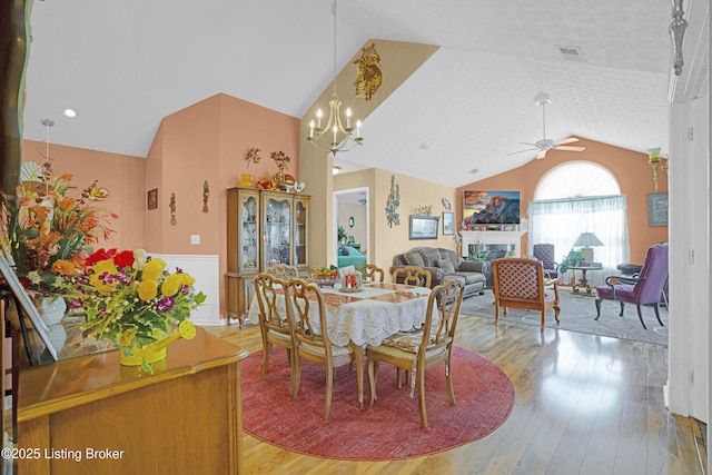 dining area featuring lofted ceiling, ceiling fan, light wood-type flooring, a chandelier, and a wainscoted wall