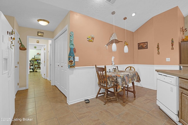 kitchen featuring dishwasher, light tile patterned flooring, wainscoting, lofted ceiling, and pendant lighting