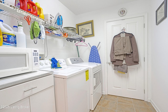 clothes washing area with washing machine and clothes dryer, light tile patterned floors, and baseboards