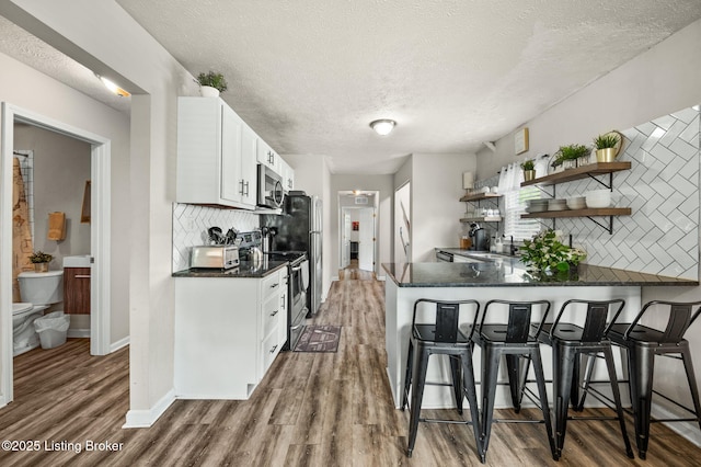 1136 Euclid Ave, Louisville, KY 40208 - kitchen with stainless steel appliances, dark countertops, a textured ceiling, open shelves, and decorative backsplash