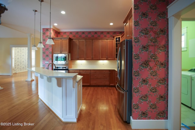 kitchen with appliances with stainless steel finishes, light countertops, light wood finished floors, washing machine and dryer, and a kitchen bar