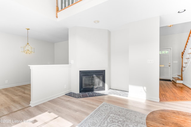 unfurnished living room with stairway, wood finished floors, a tile fireplace, baseboards, and a chandelier