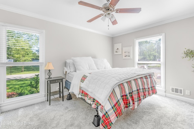 carpeted bedroom with multiple windows, ornamental molding, a ceiling fan, and baseboards