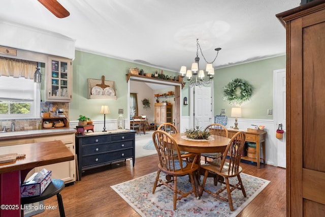 dining space featuring a chandelier, wainscoting, dark wood finished floors, crown molding, and ceiling fan