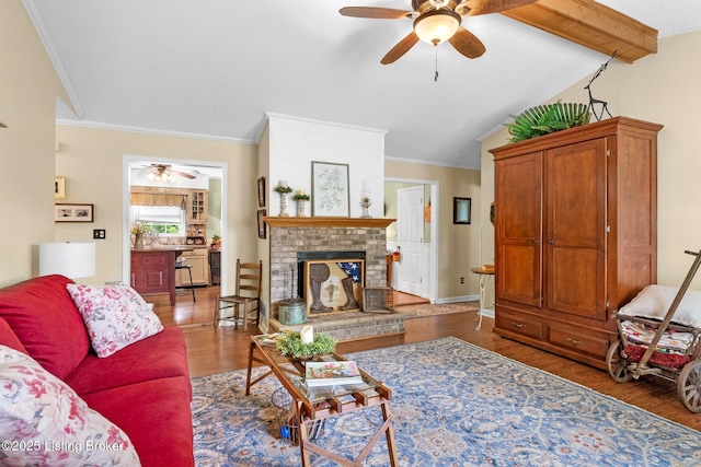 living area featuring a ceiling fan, wood finished floors, crown molding, and a brick fireplace