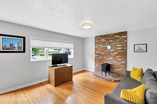 living room featuring light wood-type flooring, a wood stove, baseboards, and a textured ceiling