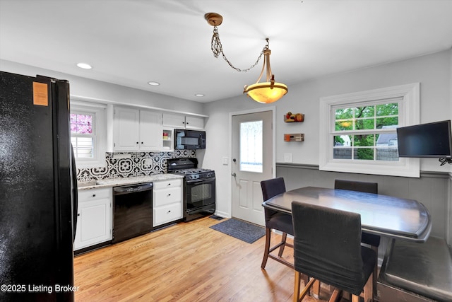 kitchen featuring black appliances, light countertops, light wood-type flooring, white cabinetry, and wainscoting