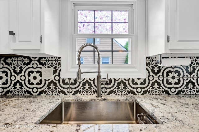 kitchen view of tasteful backsplash, a sink, white cabinetry, and light stone counters
