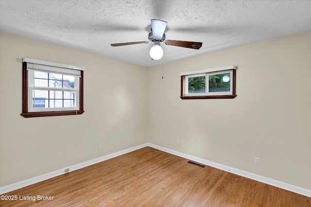 spare room with plenty of natural light, light wood-style flooring, baseboards, a textured ceiling, and ceiling fan