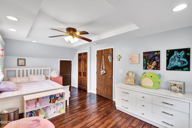 bedroom with a raised ceiling, dark wood-style floors, recessed lighting, a ceiling fan, and multiple closets