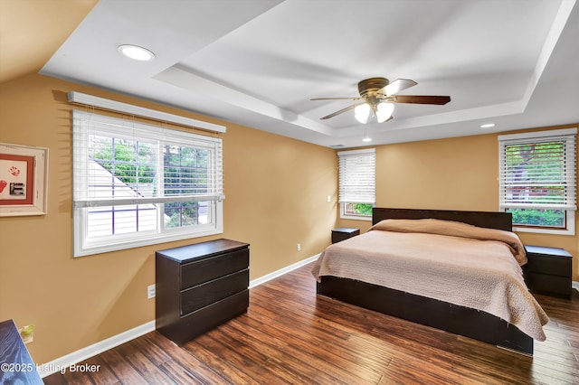 bedroom featuring a raised ceiling, dark wood-style flooring, baseboards, recessed lighting, and ceiling fan
