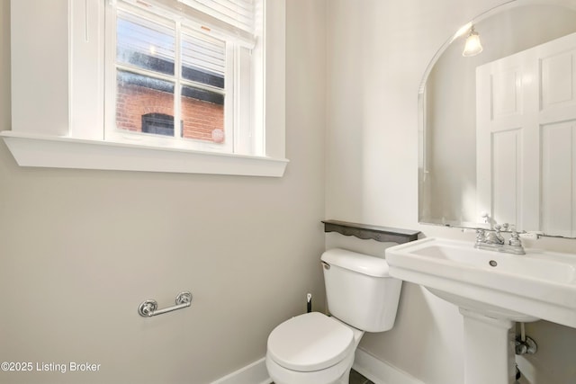 half bathroom with baseboards, toilet, and a sink