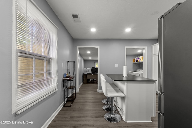 kitchen with washing machine and dryer, dark countertops, a desk, dark wood-style floors, and freestanding refrigerator