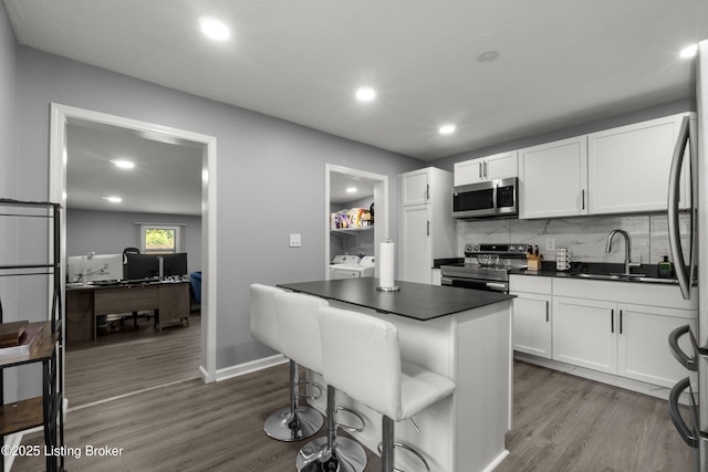 kitchen featuring stainless steel appliances, a sink, dark countertops, white cabinets, and tasteful backsplash