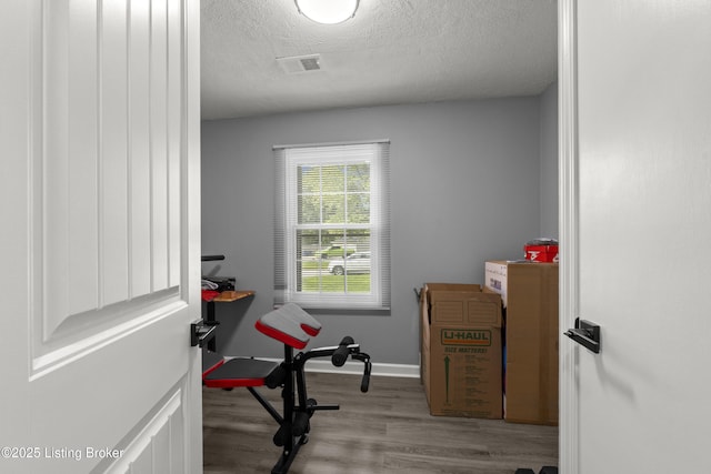 exercise area featuring a textured ceiling, wood finished floors, and baseboards