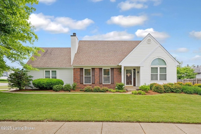 view of front of house with a front yard, brick siding, a shingled roof, and a chimney