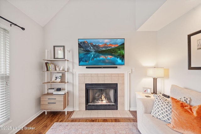 living room featuring lofted ceiling, wood finished floors, a fireplace, and baseboards