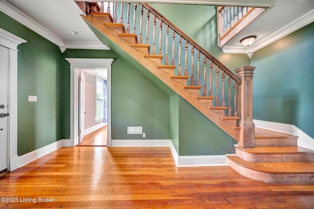 staircase featuring wood finished floors, ornamental molding, and baseboards