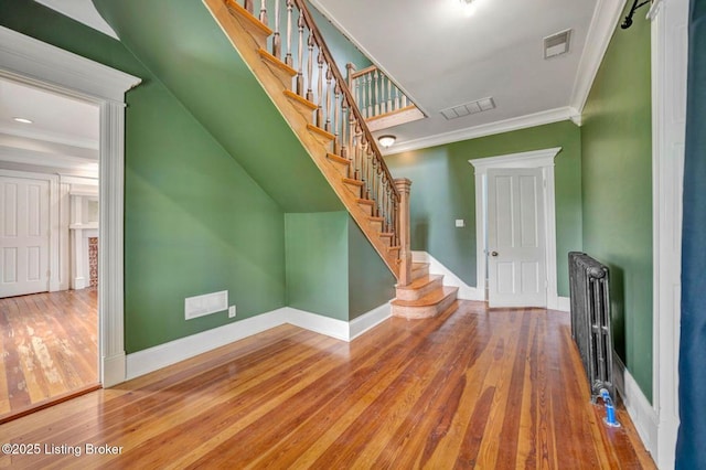 unfurnished living room featuring hardwood / wood-style floors, baseboards, ornamental molding, radiator, and stairs