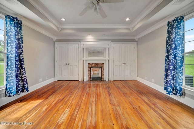 unfurnished living room featuring a raised ceiling, wood-type flooring, crown molding, baseboards, and ceiling fan