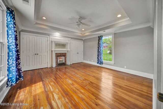 unfurnished living room featuring a raised ceiling, ceiling fan, a premium fireplace, wood-type flooring, and baseboards