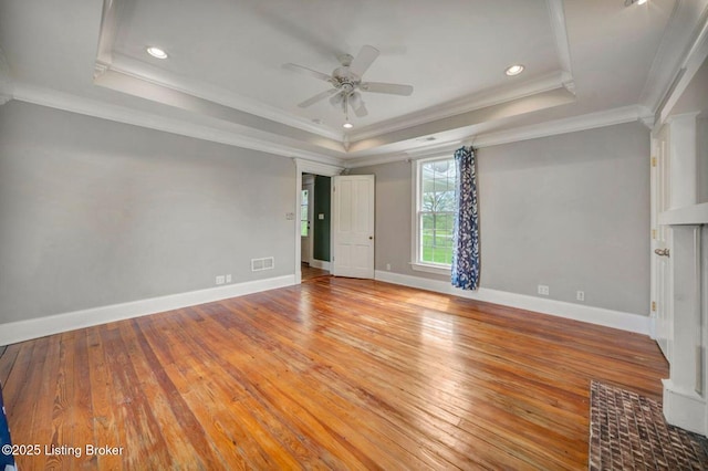 empty room with a raised ceiling, ceiling fan, light wood-style flooring, baseboards, and ornamental molding