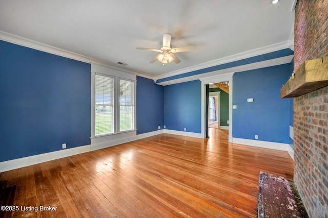 unfurnished living room featuring a ceiling fan, wood-type flooring, a brick fireplace, crown molding, and baseboards