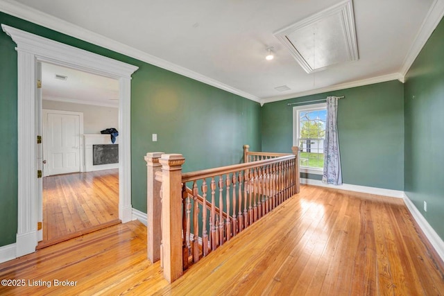 corridor with attic access, an upstairs landing, wood-type flooring, baseboards, and crown molding