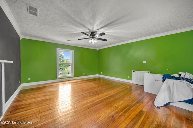 spare room featuring hardwood / wood-style flooring, a ceiling fan, a textured ceiling, ornamental molding, and baseboards