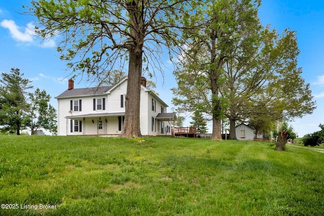 rear view of house with a chimney, a lawn, and a wooden deck