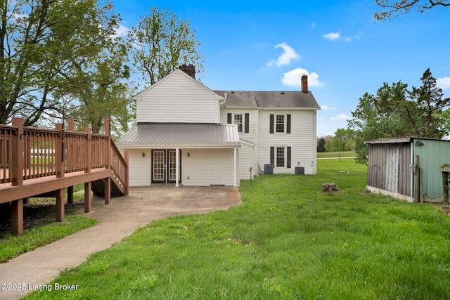 back of property featuring a lawn, a wooden deck, an outbuilding, a storage unit, and a chimney