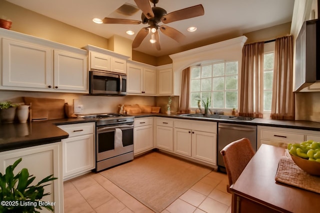 kitchen with stainless steel appliances, dark countertops, white cabinets, light tile patterned flooring, and ceiling fan