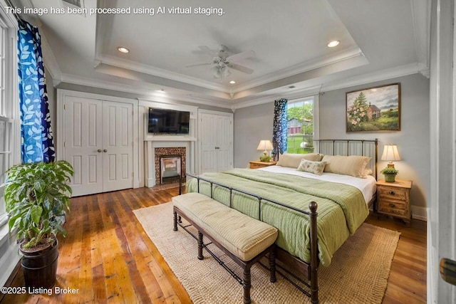 bedroom with a tray ceiling, hardwood / wood-style flooring, a premium fireplace, crown molding, and two closets