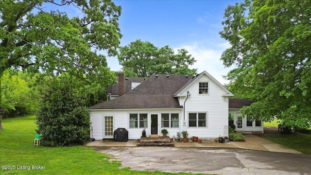 rear view of house featuring a lawn, a chimney, roof with shingles, and a patio area