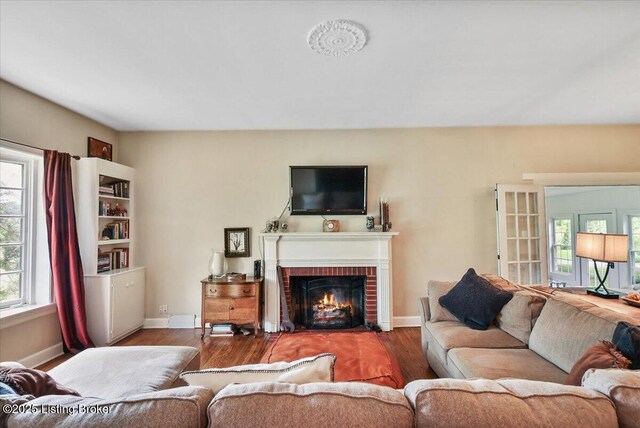 living room with wood finished floors, baseboards, and a brick fireplace