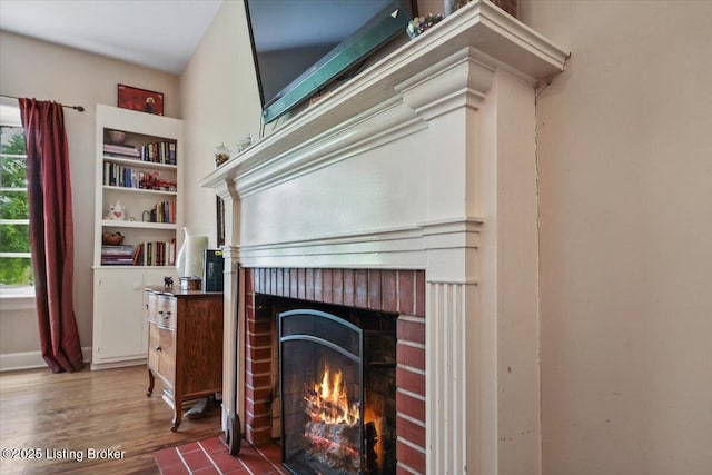 detailed view of a brick fireplace, wood finished floors, and baseboards