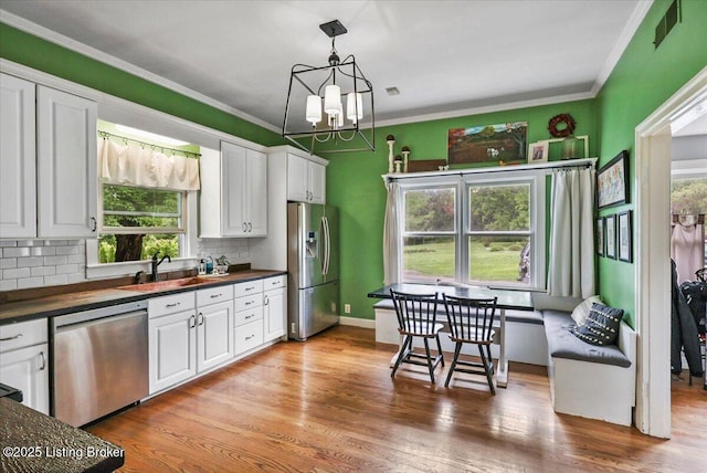 kitchen featuring stainless steel appliances, a sink, dark countertops, plenty of natural light, and ornamental molding