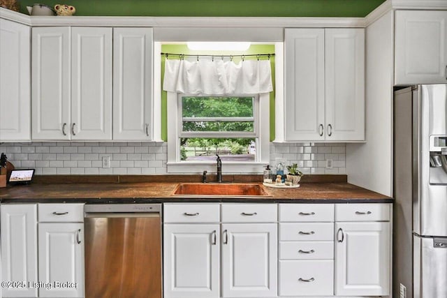 kitchen featuring stainless steel appliances, a sink, dark countertops, and white cabinetry